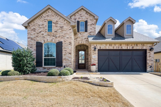 french provincial home with brick siding, concrete driveway, and an attached garage