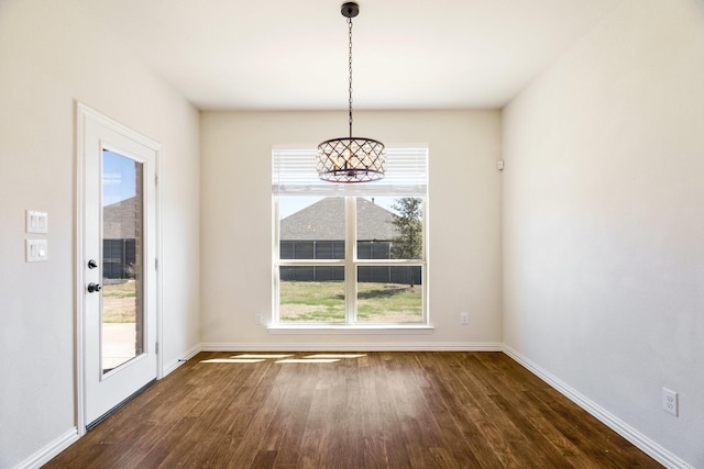 unfurnished dining area featuring a notable chandelier, baseboards, and dark wood-style flooring