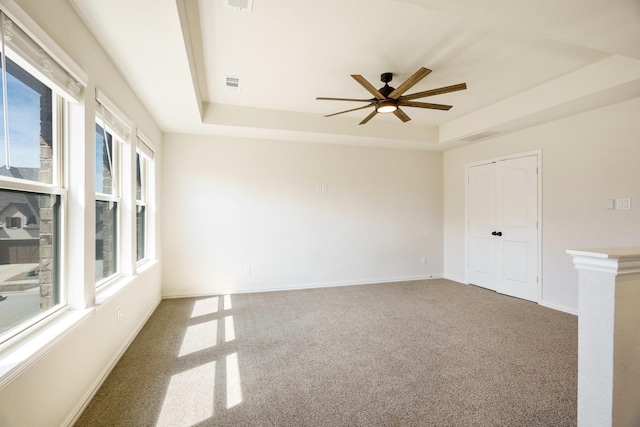 carpeted empty room with visible vents, a raised ceiling, baseboards, and ceiling fan