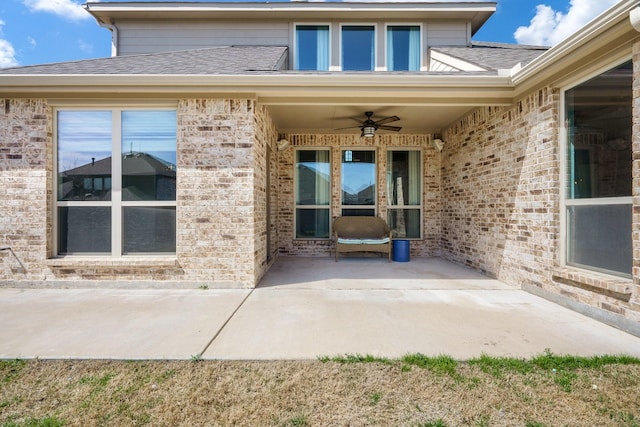 view of exterior entry featuring a patio, brick siding, roof with shingles, and ceiling fan