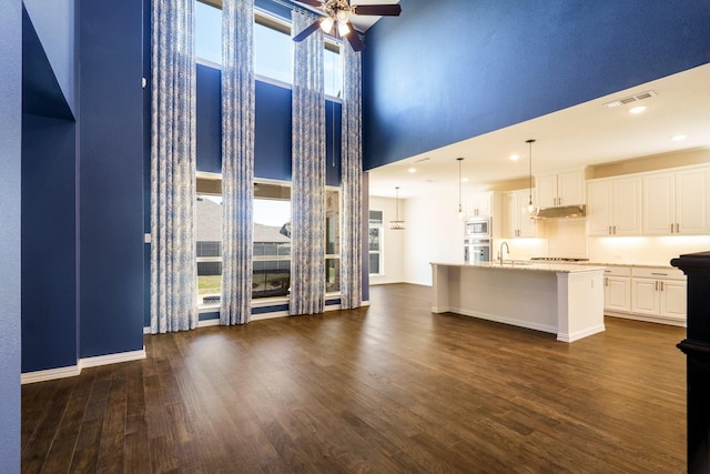 kitchen featuring dark wood-type flooring, an island with sink, white cabinetry, light countertops, and ceiling fan