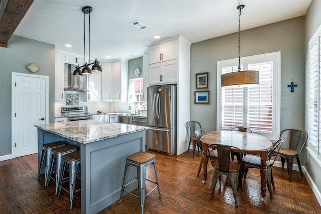 kitchen featuring visible vents, stainless steel appliances, decorative backsplash, a kitchen bar, and a center island