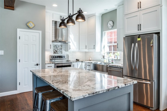 kitchen with wall chimney range hood, backsplash, light stone countertops, and appliances with stainless steel finishes