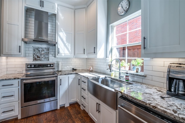 kitchen featuring a sink, wall chimney range hood, white cabinets, and stainless steel appliances