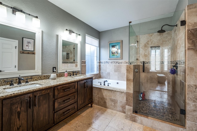 full bathroom featuring stone tile floors, a shower stall, a garden tub, and a sink