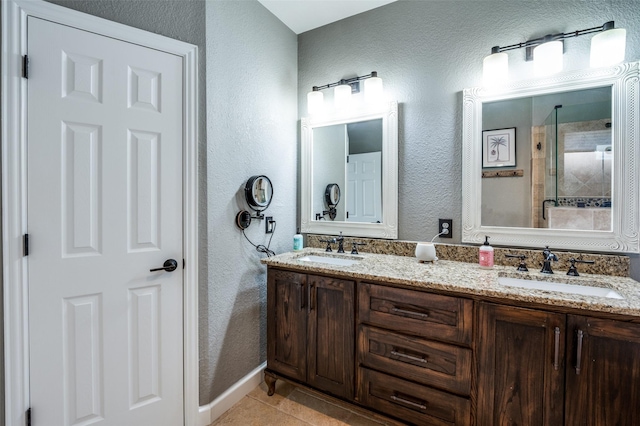 bathroom featuring a shower stall, a textured wall, double vanity, and a sink