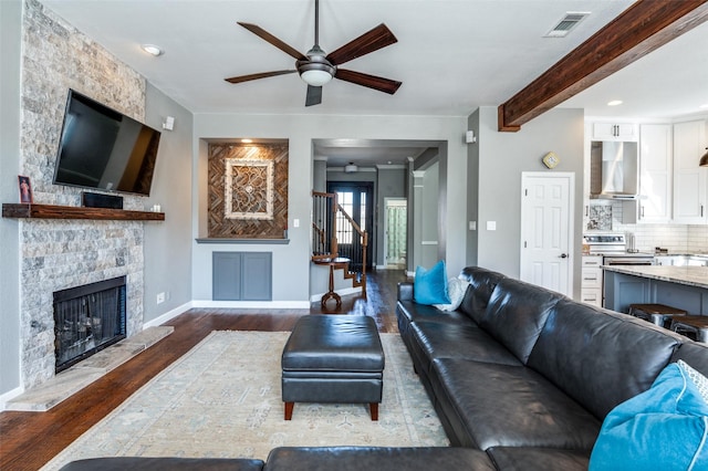 living area featuring visible vents, stairs, beam ceiling, a fireplace, and wood finished floors