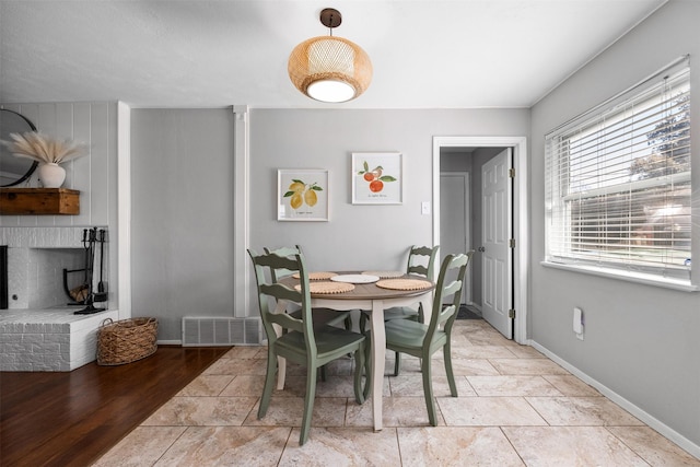 dining space with light tile patterned floors, visible vents, a brick fireplace, and baseboards