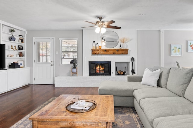 living room featuring a ceiling fan, a brick fireplace, and dark wood-style floors