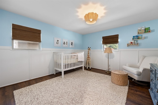 bedroom featuring a wainscoted wall, a crib, and wood finished floors