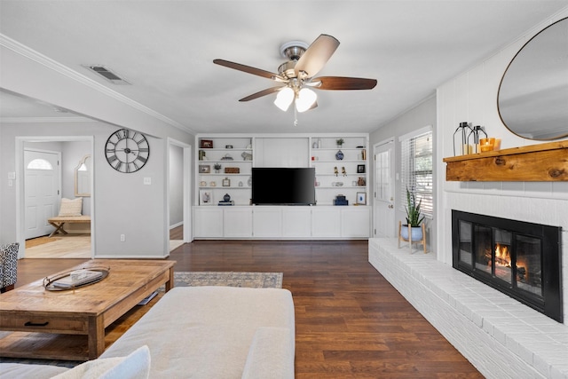 living room featuring built in features, wood finished floors, visible vents, a fireplace, and ornamental molding