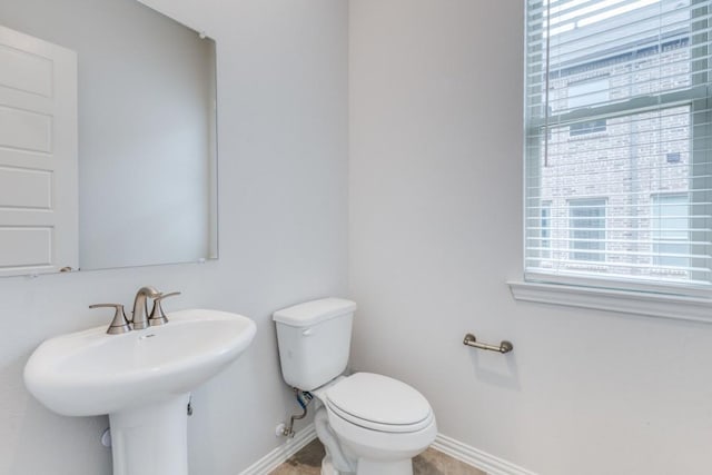 half bath featuring toilet, baseboards, and a sink