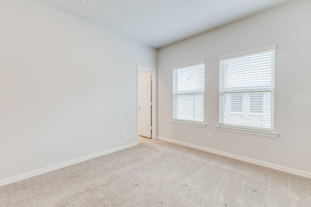 spare room with baseboards and light colored carpet