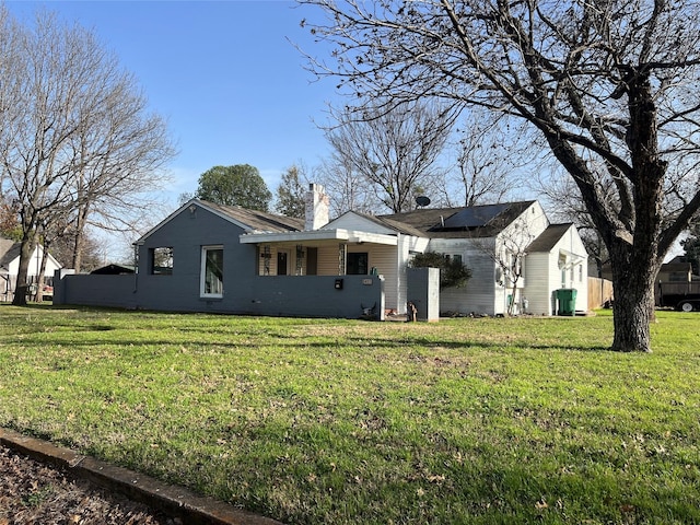 exterior space with roof mounted solar panels, a chimney, and a front lawn