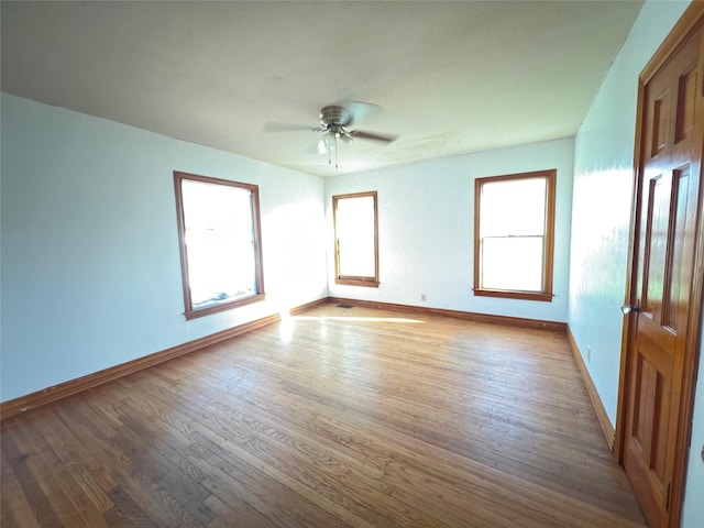 spare room featuring plenty of natural light, ceiling fan, baseboards, and wood finished floors