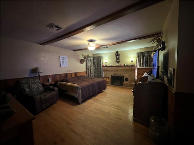 bedroom featuring visible vents, beamed ceiling, wood finished floors, and a wainscoted wall