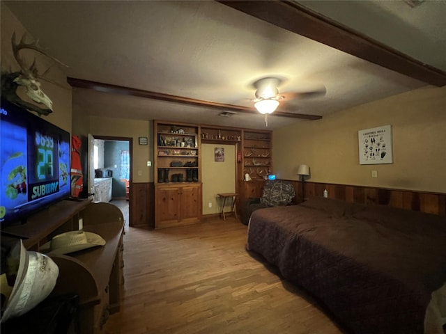 bedroom featuring light wood-style flooring, wooden walls, a ceiling fan, and a wainscoted wall