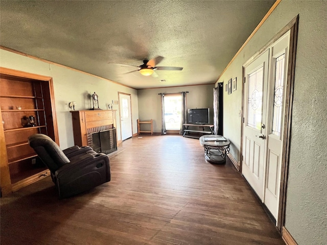 living area featuring wood finished floors, a fireplace, ceiling fan, a textured ceiling, and crown molding