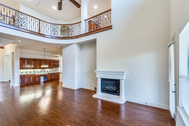 unfurnished living room featuring a glass covered fireplace, baseboards, a high ceiling, and dark wood finished floors