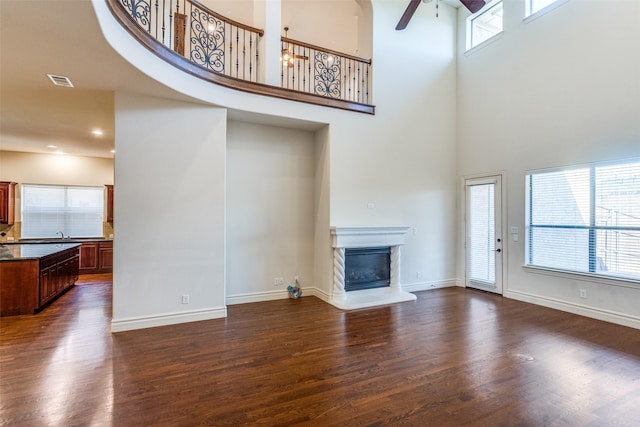 living room featuring visible vents, dark wood-type flooring, a ceiling fan, a glass covered fireplace, and baseboards