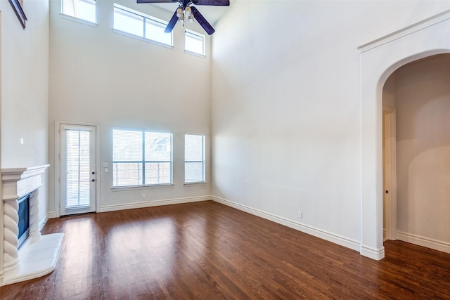 unfurnished living room featuring ceiling fan, a premium fireplace, baseboards, and wood finished floors