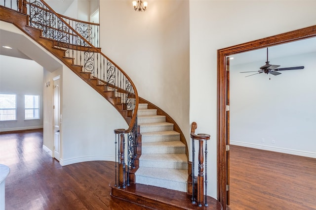 stairway with ceiling fan with notable chandelier, a high ceiling, baseboards, and wood finished floors