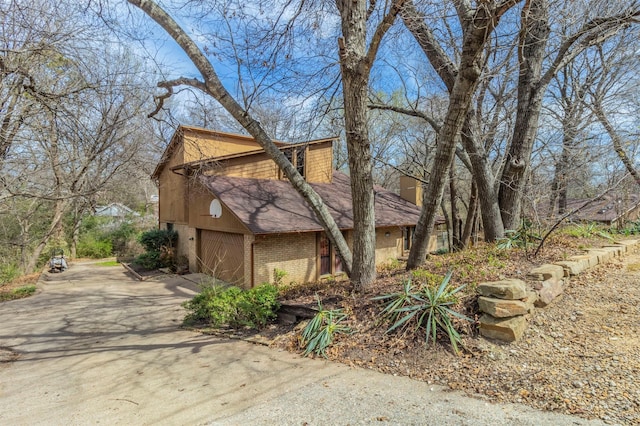 view of property exterior with brick siding, driveway, a shingled roof, and a garage