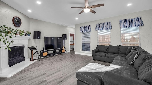 living room with recessed lighting, a fireplace with raised hearth, a ceiling fan, and wood finished floors