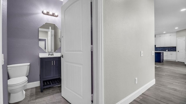 bathroom featuring vanity, wood finished floors, baseboards, toilet, and backsplash