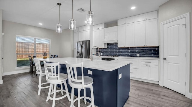 kitchen with a center island with sink, custom range hood, decorative backsplash, a kitchen breakfast bar, and stainless steel fridge