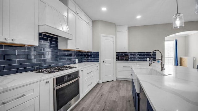 kitchen with white cabinets, arched walkways, premium range hood, and appliances with stainless steel finishes