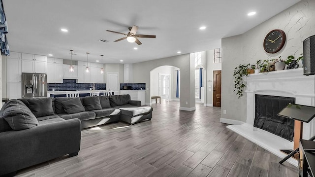 living room featuring wood finished floors, visible vents, recessed lighting, arched walkways, and a glass covered fireplace