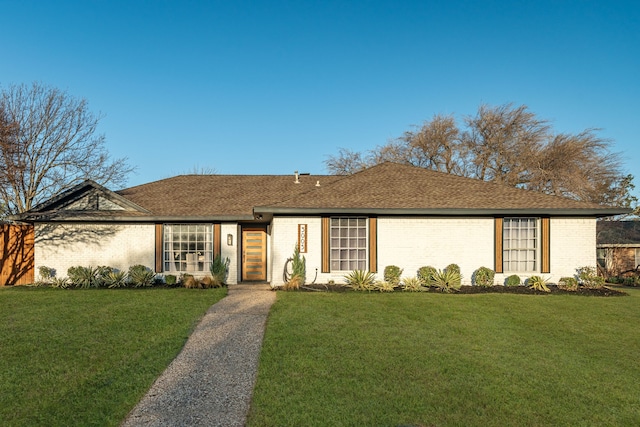 ranch-style house featuring brick siding, a front yard, and roof with shingles