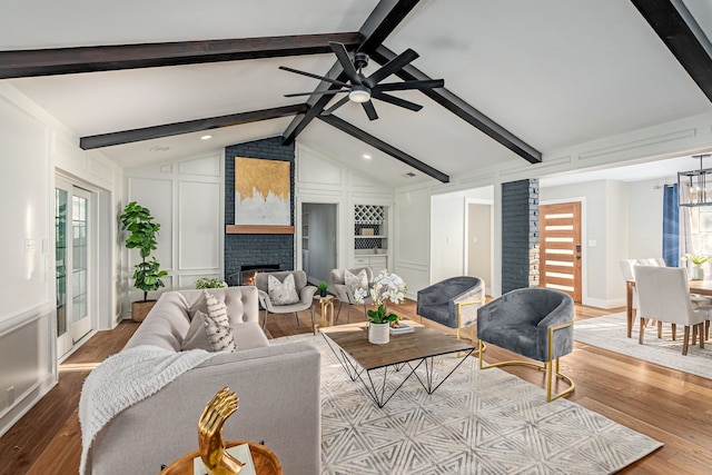 living area with a ceiling fan, wood finished floors, a decorative wall, a brick fireplace, and vaulted ceiling with beams