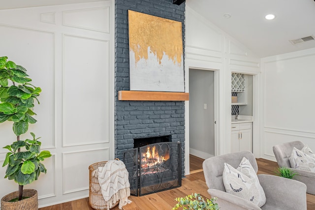 living area with visible vents, wood finished floors, a fireplace, a decorative wall, and vaulted ceiling