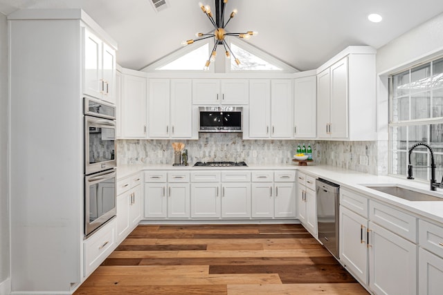 kitchen with stainless steel appliances, a sink, vaulted ceiling, white cabinets, and a chandelier