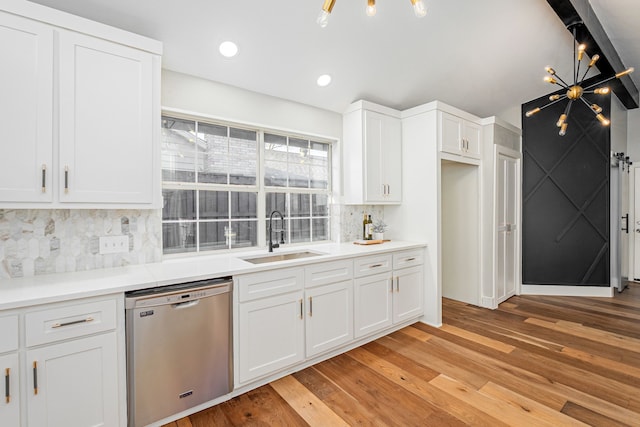 kitchen featuring tasteful backsplash, stainless steel dishwasher, light wood-style floors, white cabinetry, and a sink