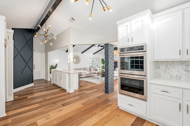 kitchen with stainless steel double oven, lofted ceiling with beams, decorative backsplash, a notable chandelier, and open floor plan