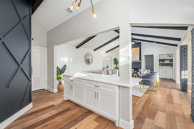 kitchen featuring visible vents, white cabinetry, vaulted ceiling with beams, and light wood-type flooring