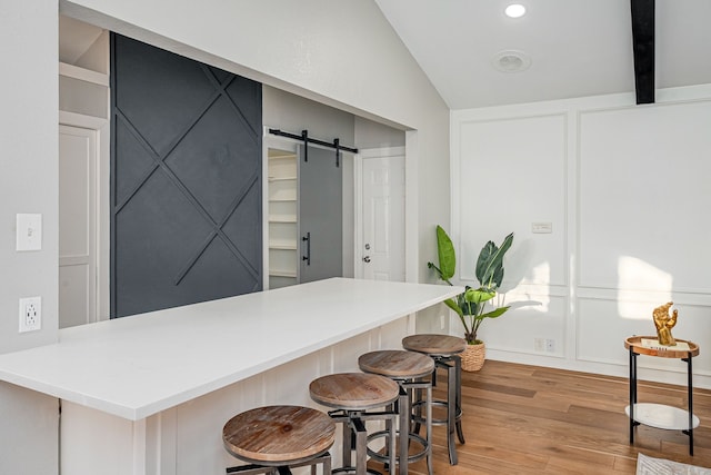 kitchen featuring vaulted ceiling with beams, a breakfast bar, a barn door, light wood-style floors, and a decorative wall