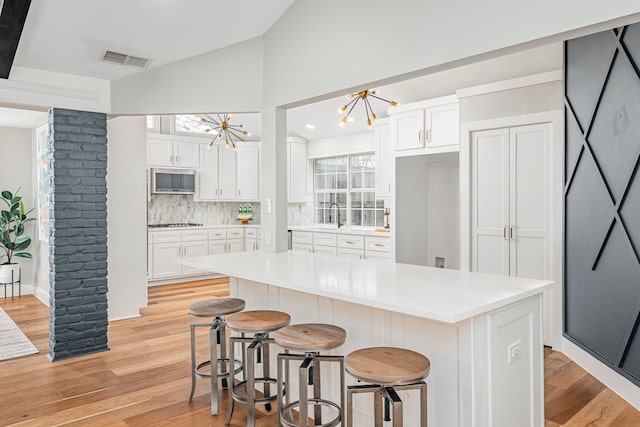 kitchen with stainless steel microwave, visible vents, vaulted ceiling, a notable chandelier, and gas stovetop