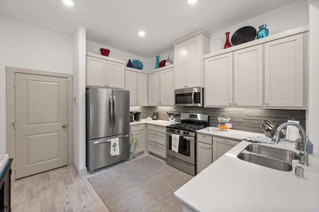 kitchen with light wood-type flooring, light countertops, decorative backsplash, stainless steel appliances, and a sink