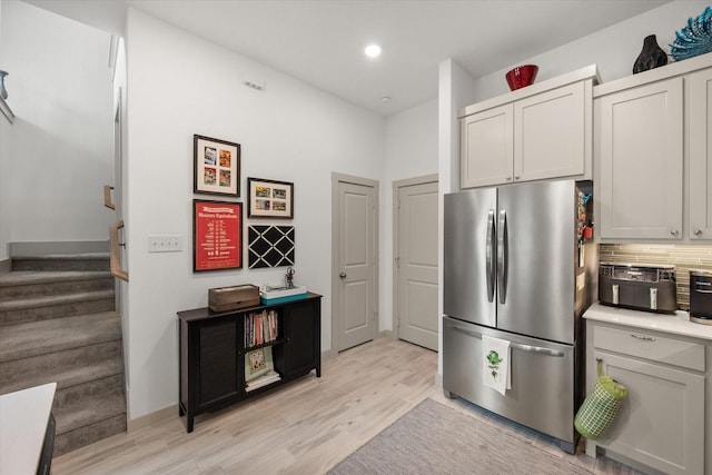 kitchen with freestanding refrigerator, recessed lighting, light wood finished floors, decorative backsplash, and light countertops