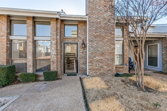 view of exterior entry featuring brick siding and a chimney