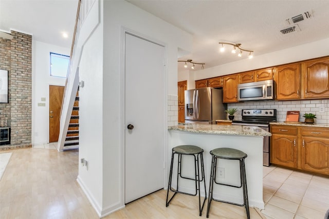 kitchen with stainless steel appliances, tasteful backsplash, visible vents, and brown cabinetry