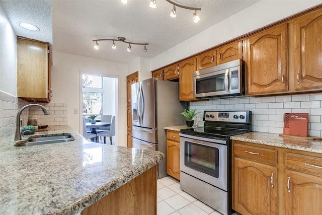 kitchen featuring light tile patterned floors, stainless steel appliances, brown cabinetry, a textured ceiling, and a sink