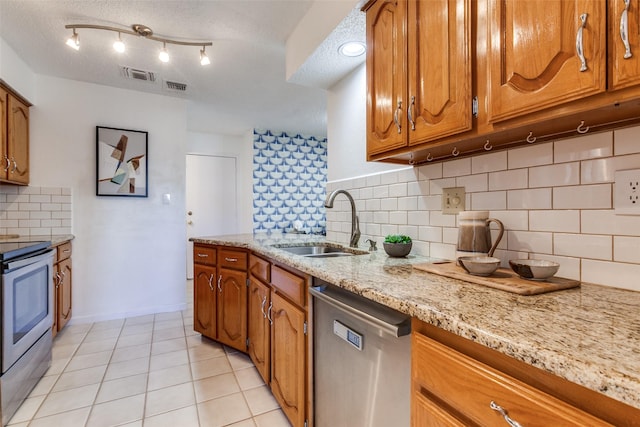 kitchen featuring light tile patterned floors, visible vents, a sink, stainless steel appliances, and brown cabinets