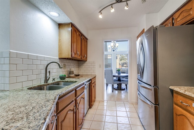 kitchen featuring backsplash, appliances with stainless steel finishes, brown cabinetry, a notable chandelier, and a sink