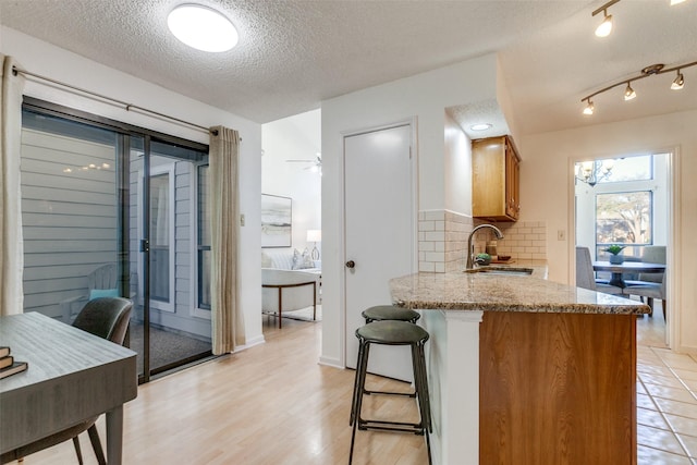 kitchen featuring backsplash, a breakfast bar, light stone counters, brown cabinetry, and a sink