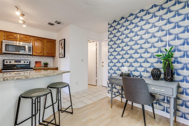 kitchen featuring a textured ceiling, tasteful backsplash, appliances with stainless steel finishes, and light wood finished floors